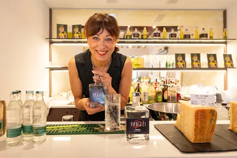 Cristina Parizzi dietro il bancone dell'aperitivo, fra bottiglie e prodotti selezionati