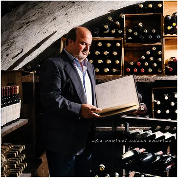 Ugo Parizzi in cantina, fra le bottiglie, mentre consulta il registro dei vini